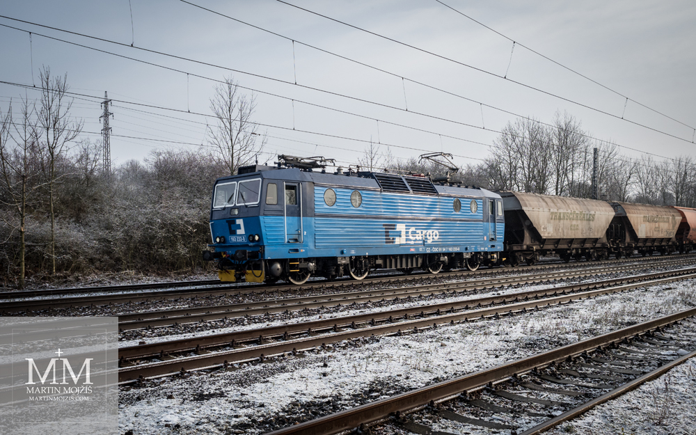 Elektrická lokomotiva v čele vlaku přepravujícího obilí. Fotografie vytvořena objektivem Olympus 12 - 40 mm 2.8 Pro.